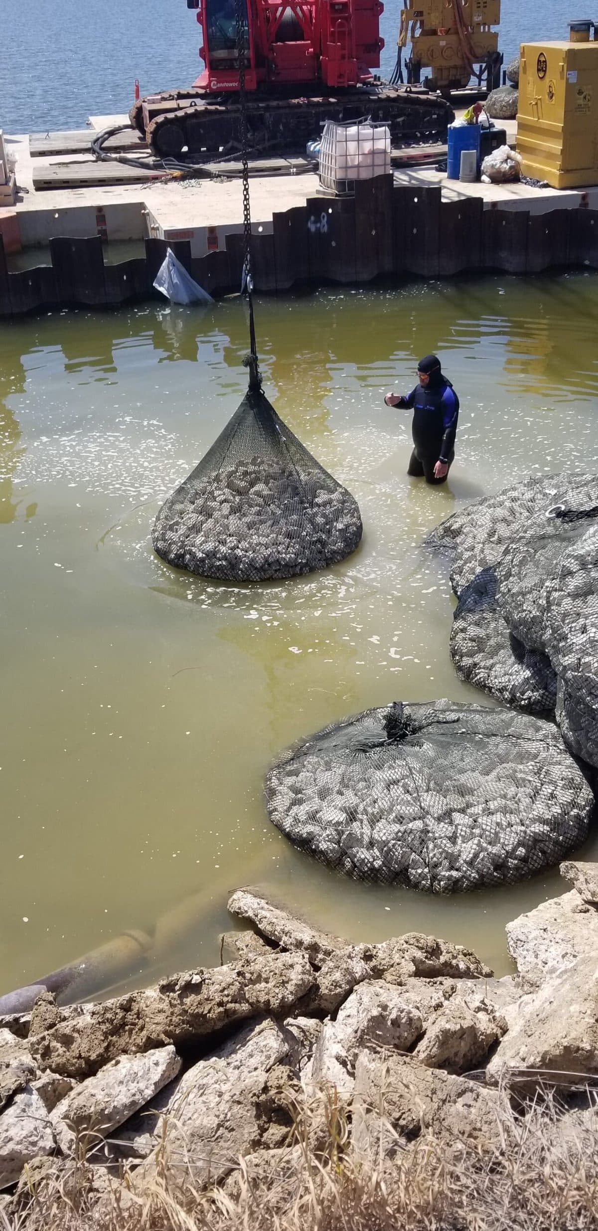 A filled rock bag being lowered into the water by crane
